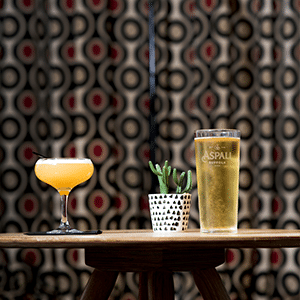 Cocktail and beer on top of table with small plant